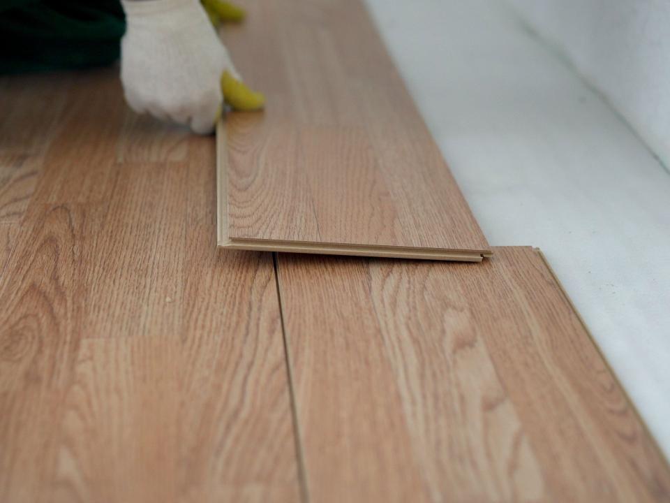 A person installing wood-effect laminate flooring in a room with a concrete floor.