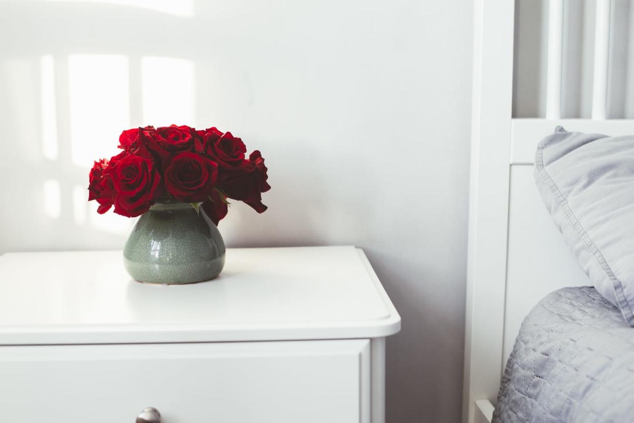 red roses in vase on white bedside table by wall at home