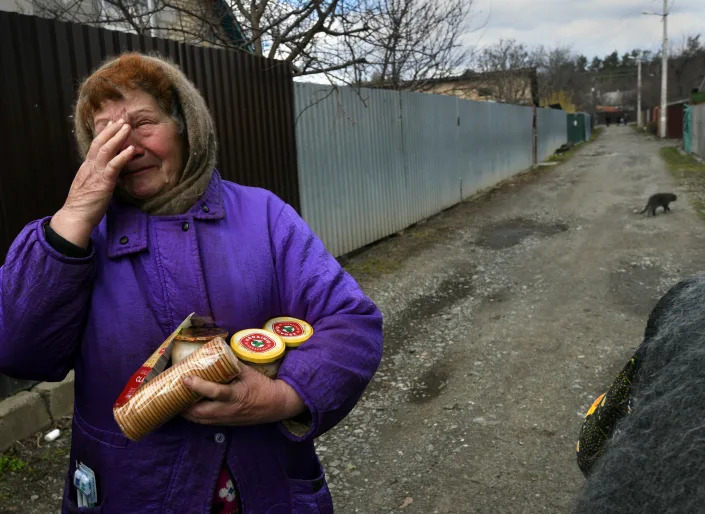 Обезумевшая женщина в пурпурном пальто и шерстяном платке несет продовольственную помощь, в том числе крекеры, розданные в Буче.