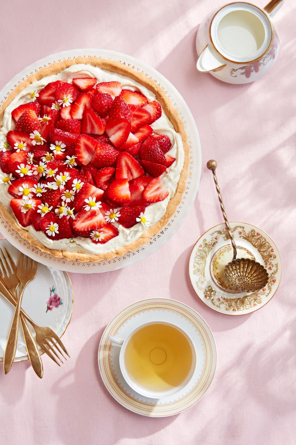 chamomile mascarpone tart with fresh strawberries and chamomile flower garnish on a pink tablecloth, with a cup of tea