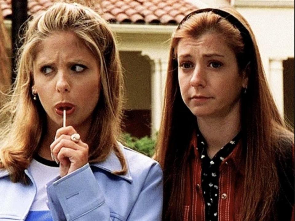 Two people, Sarah Michelle Gellar and Alyson Hannigan, are seen in an outside setting; Gellar is sucking on a lollipop while Hannigan has a concerned look