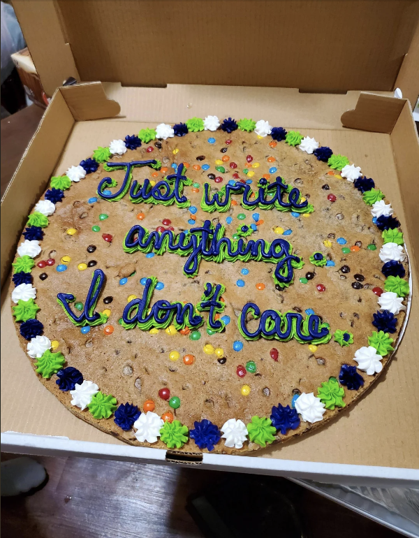 Large cookie cake with colorful icing that reads, "Just write anything I don't care," surrounded by small blue, green, white, and black icing decorations