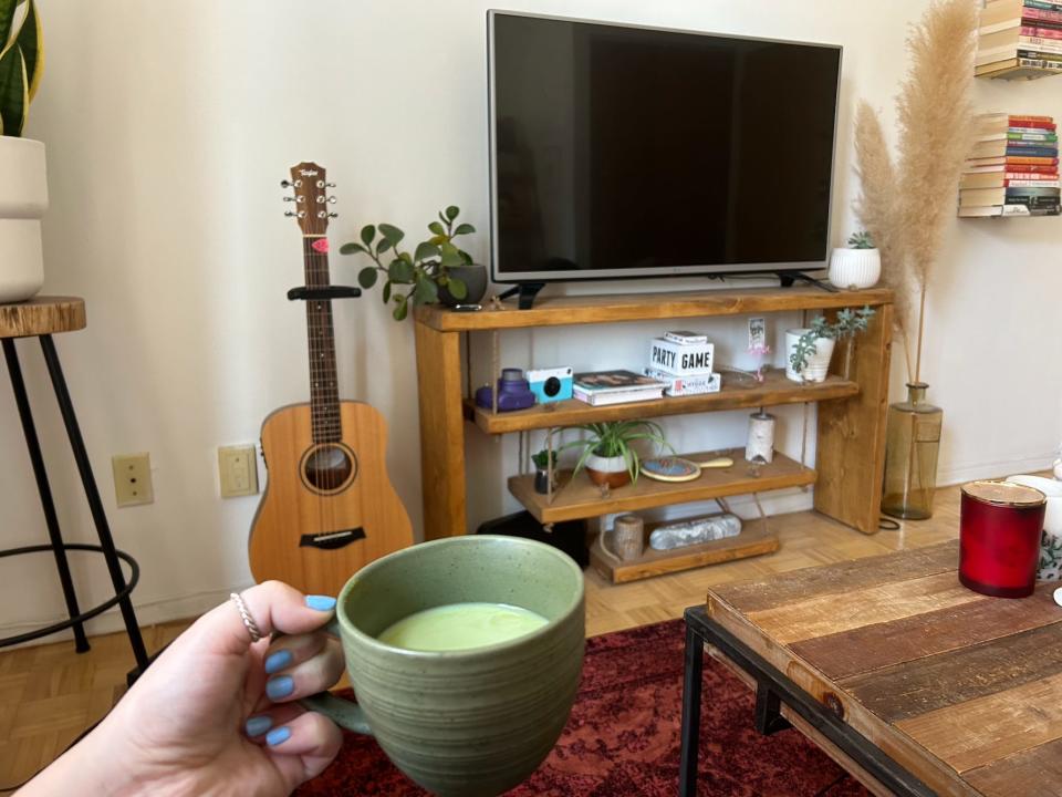 hand holding a mug of matcha latte in a living room