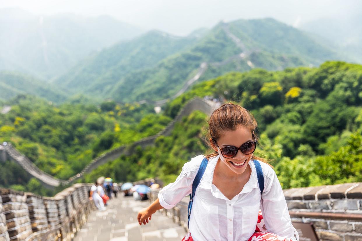 Smiling woman walking along the Great Wall in Badaling north of Beijing, she is shown along the bottom of image, with the great expanse of the wall and mountains