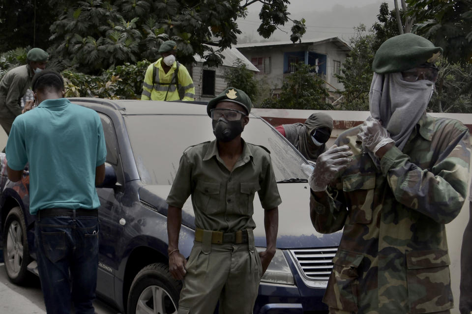 Soldiers and residents stand next to a car covered in volcanic ash in Kingstown, on the eastern Caribbean island of St. Vincent, Saturday, April 10, 2021, due to the eruption of the La Soufriere volcano. (AP Photo/Orvil Samuel)