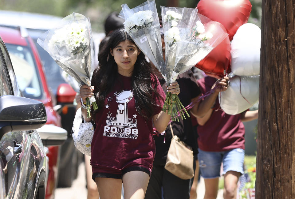 Mourners bring flowers and balloons to pay their respects to the 21 victims of the Robb Elementary School shooting in Uvalde, Texas, Thursday, May 26, 2022. Wooden crosses have been placed near the school marquee which has been a memorial site. (Kin Man Hui/The San Antonio Express-News via AP)