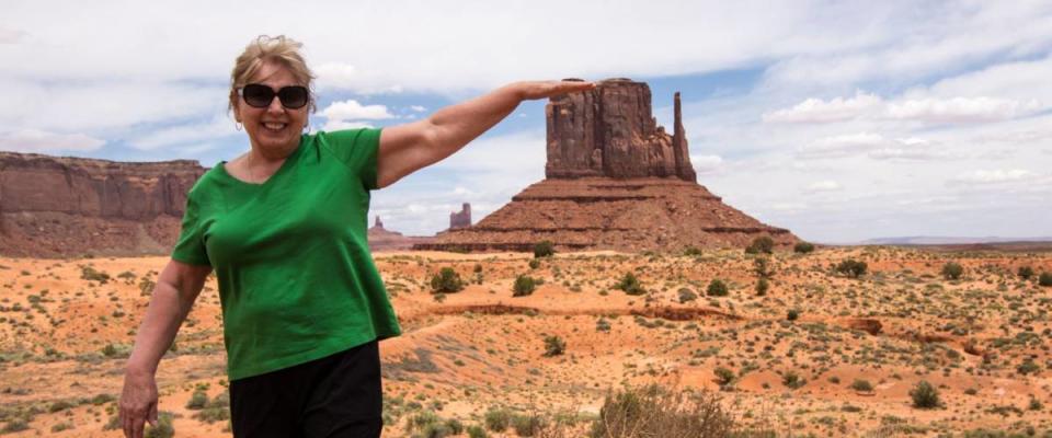 Forced perspective of a senior adult woman (60s) pretending to touch a famous rock formation in Utah Monument Valley