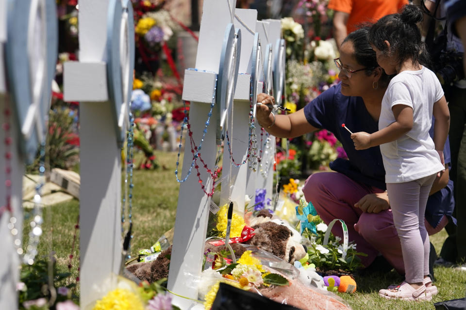 A womand signs a cross as a child looks on at a makeshift memorial by the mall where several people were killed in Saturday's mass shooting, Monday, May 8, 2023, in Allen, Texas. (AP Photo/Tony Gutierrez)