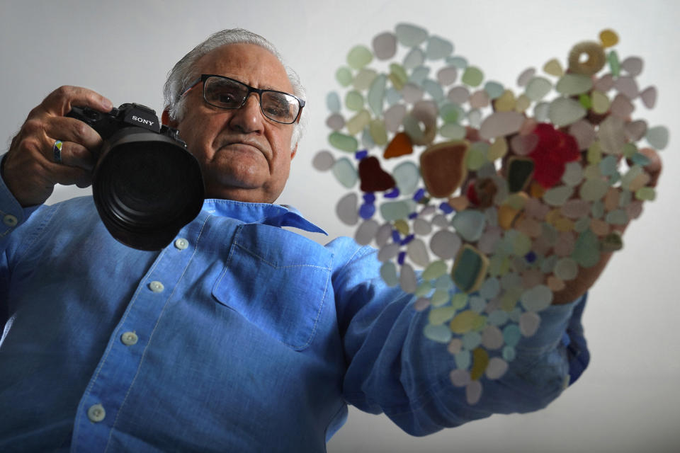 Donald Verger arranges sea glass in the shape of a heart, Thursday, Feb. 11, 2021, in Falmouth, Maine. After photographing his art, Verger donates photos and cards to schools and hospitals as a way of giving back during the pandemic. (AP Photo/Robert F. Bukaty)