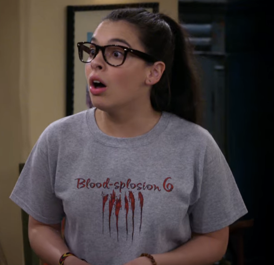 Woman in glasses and a T-shirt with "Blood-splosion 6" text and graphic. She looks surprised