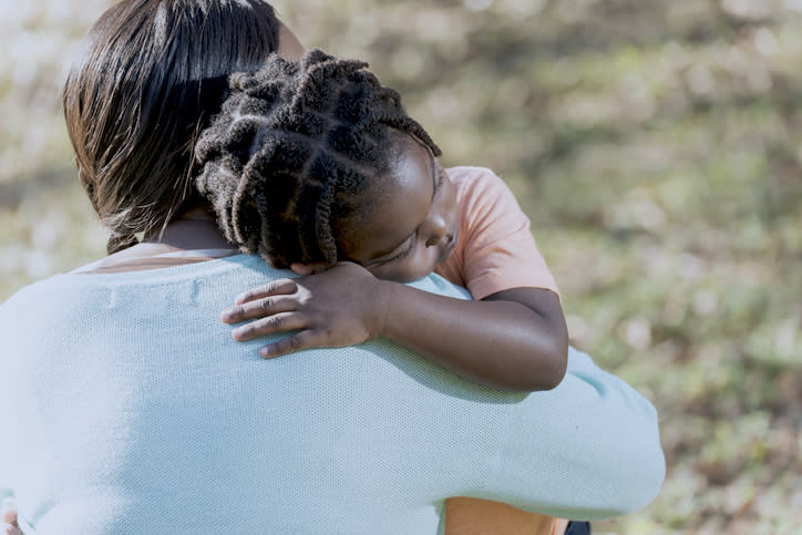 Woman holding child, both with backs turned, sharing a tender embrace outdoors