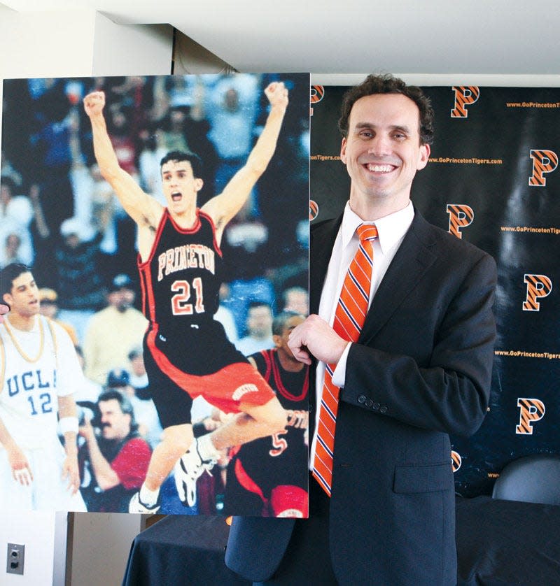 Princeton coach Mitch Henderson holds up the iconic photo of him as a Princeton player after beating No. 4 defending champions UCLA in the first round of the 1996 NCAA tournament.