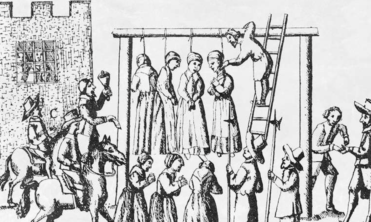 Four women hang from the gallows, and a man checks the pulse of one of them. Meanwhile, townspeople surround the gallows and watch.