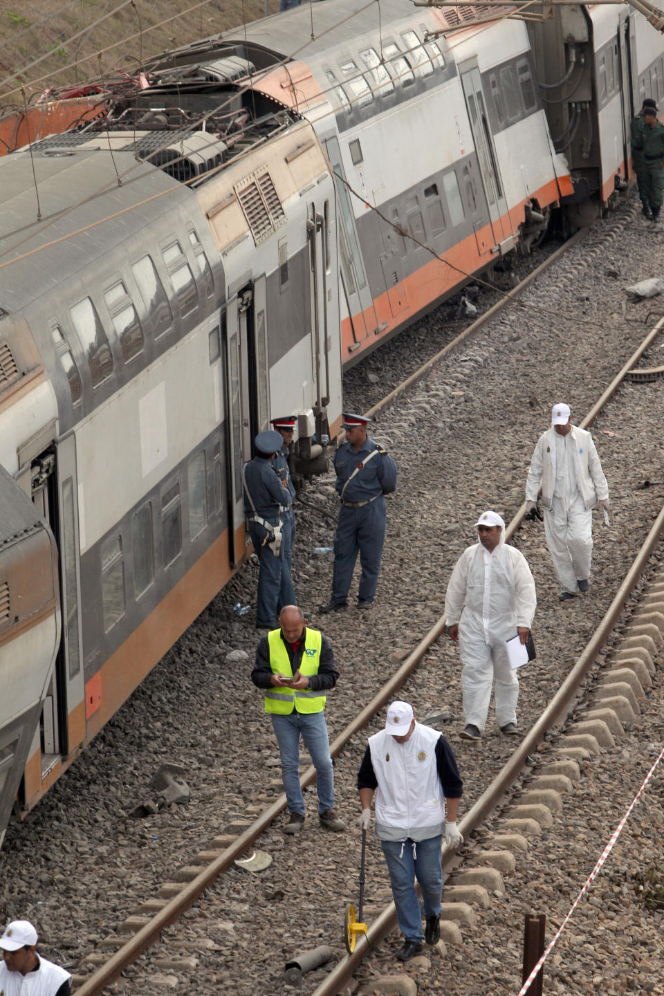 Police officers and rail workers stand by a derailed train Tuesday Oct.16, 2018 near Sidi Bouknadel, Morocco. A shuttle train linking the Moroccan capital Rabat to a town further north on the Atlantic coast derailed Tuesday, killing several people and injuring dozens, Moroccan authorities and the state news agency said. (AP Photo/Abdeljalil Bounhar)