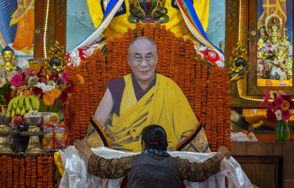 A woman offers a ceremonial scarf in front of a portrait of her spiritual leader the Dalai Lama during his 88th birthday celebration in Kathmandu, Nepal, Thursday, July 6, 2023. (AP Photo/Niranjan Shrestha)
