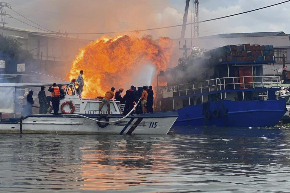 In this photo provided by the Philippine Coast Guard, members of the Philippine Coast Guard try to extinguish flames on a burning cargo ship docked in Manila, Philippines, Saturday, June 12, 2021. The fire and a powerful blast ripped through ship docked to refuel in the Philippine capital of Manila on Saturday, injuring at least six people and igniting a blaze in a nearby riverside slum that gutted dozens of shanties, officials said. (Philippine Coast Guard via AP)