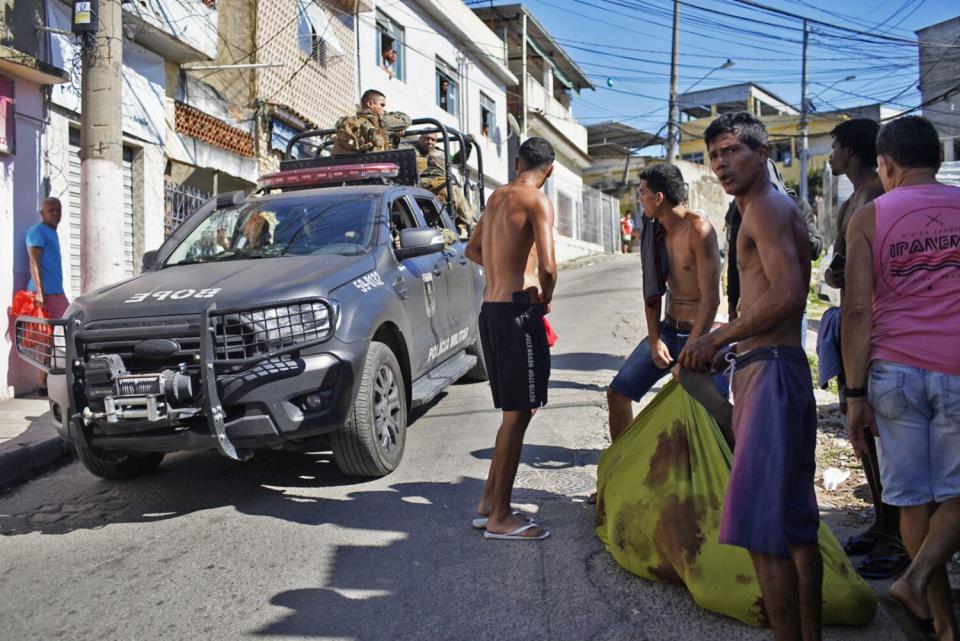 A truck passes people carrying a body.