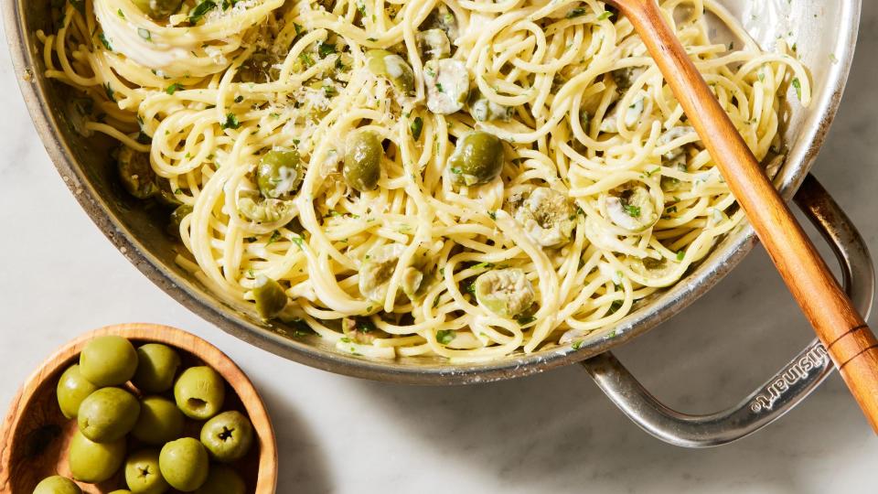 a pot of cooked spaghetti in a cream sauce with pieces of green olive, chopped parsley, and parmesan