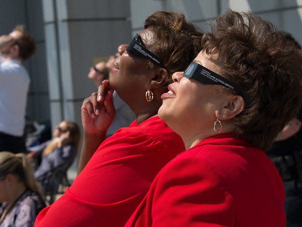 Two women in red shirts wearing square sunglasses look at the sunlight