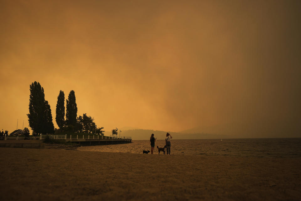 Smoke from the McDougall Creek wildfire fills the air and nearly blocks out the sun as people take in the view of Okanagan Lake from Tugboat Beach, in Kelowna, British Columbia, Friday, Aug. 18, 2023. (Darryl Dyck/The Canadian Press via AP)