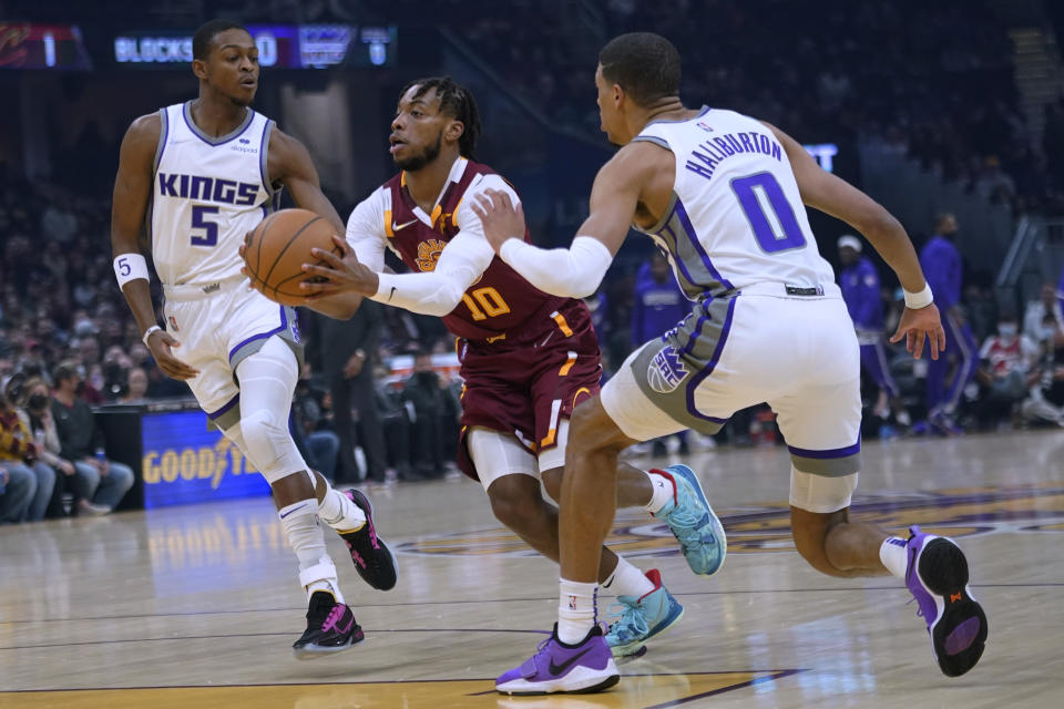 Cleveland Cavaliers' Darius Garland (10) drives between Sacramento Kings' De'Aaron Fox (5) and Tyrese Haliburton (0) during the first half of an NBA basketball game Saturday, Dec. 11, 2021, in Cleveland. (AP Photo/Tony Dejak)