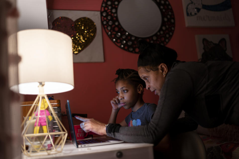 Abigail Schneider, 8, center, completes a level of her learning game with her mother April in her bedroom, Wednesday, Dec. 8, 2021, in the Brooklyn borough of New York. "I'm determined to push and push to get them the things that help them," said April Schneider. "I have to go above and beyond to make sure whatever requirements they need they get." (AP Photo/John Minchillo)
