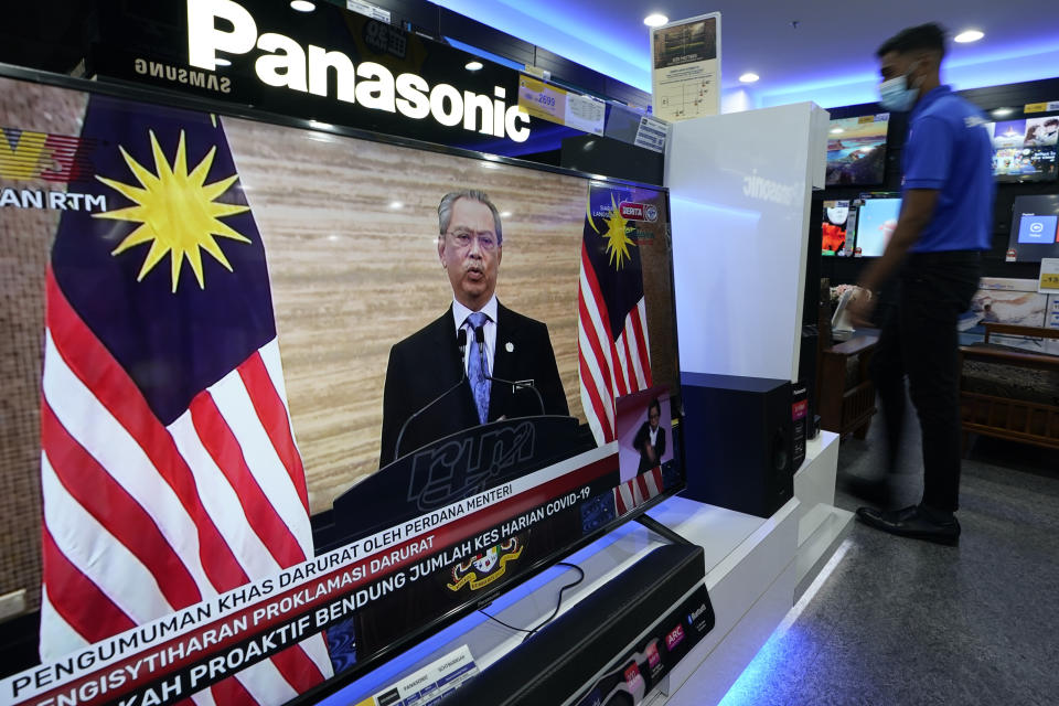 An electronic shop worker wearing a face mask walks near a television showing a live broadcast of Malaysian Prime Minister Muhyiddin Yassin at a shopping outlet in Kuala Lumpur, Malaysia, Tuesday, Jan. 12, 2021. Malaysia's king Tuesday approved a coronavirus emergency that will prorogue parliament and halt any bids to seek a general election in a political reprieve for embattled Muhyiddin. (AP Photo/Vincent Thian)