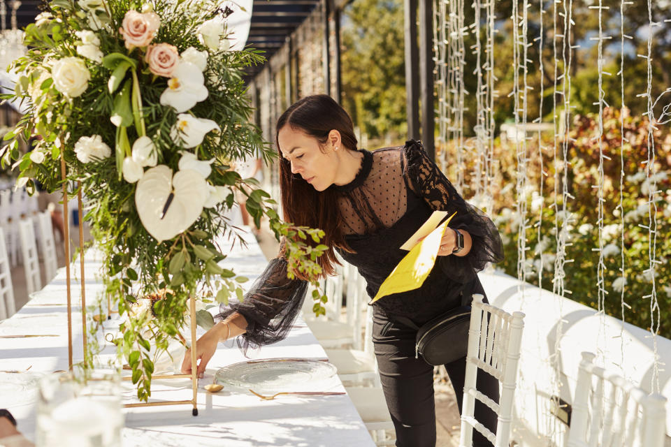 Person arranging table decorations for an event, placing a name card among flowers