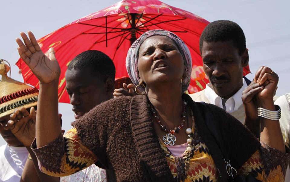 A woman from a group of churchgoers wails at the site, Sunday Aug. 19, 2012 at the Lonmin platinum mine, background, near Rustenburg, South Africa, during a memorial service for 34 dead striking miners who were shot and killed bt police last Thursday. Miners must return to work Monday or face being fired from the mine where rivalry between unions has exploded into violence. (AP Photo/Denis Farrell)