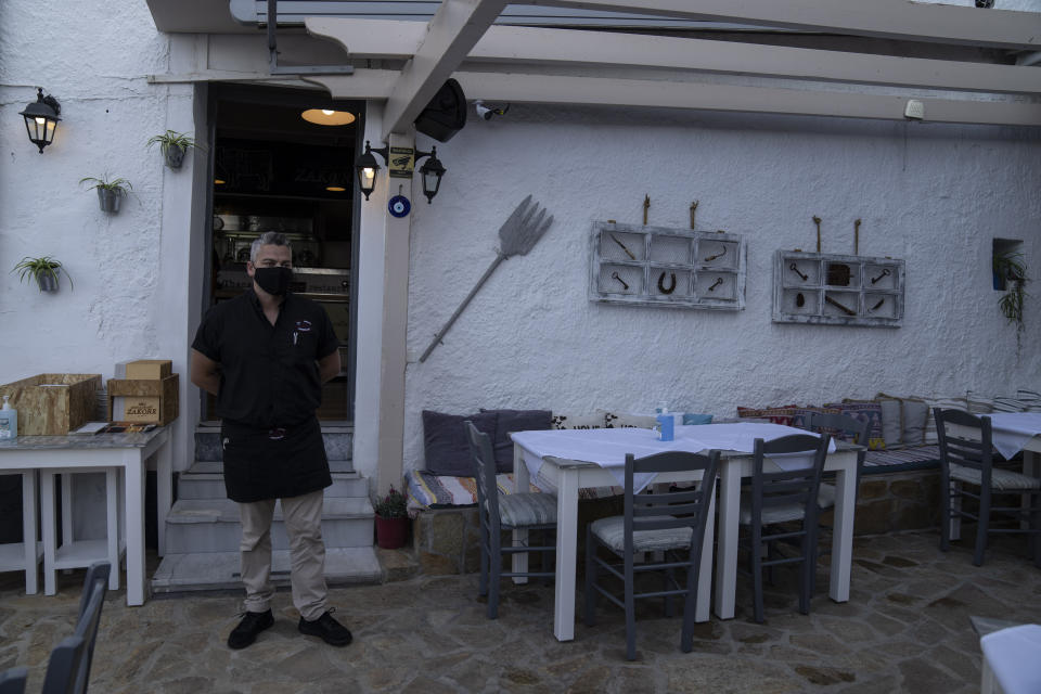 Thanassis Safis, wearing a protective face mask stands outside the restaurant that he runs in a popular spot of Kokkari harbor, on the eastern Aegean island of Samos, Greece, Tuesday, June 8, 2021. About a month after Greece officially opened to international visitors, the uncertainty of travel during a pandemic is still taking its toll on the country's vital tourist industry. (AP Photo/Petros Giannakouris)