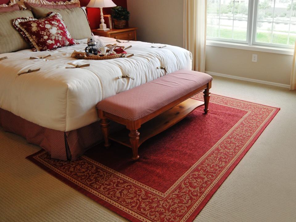 White bed in bedroom with red ottoman and red rug