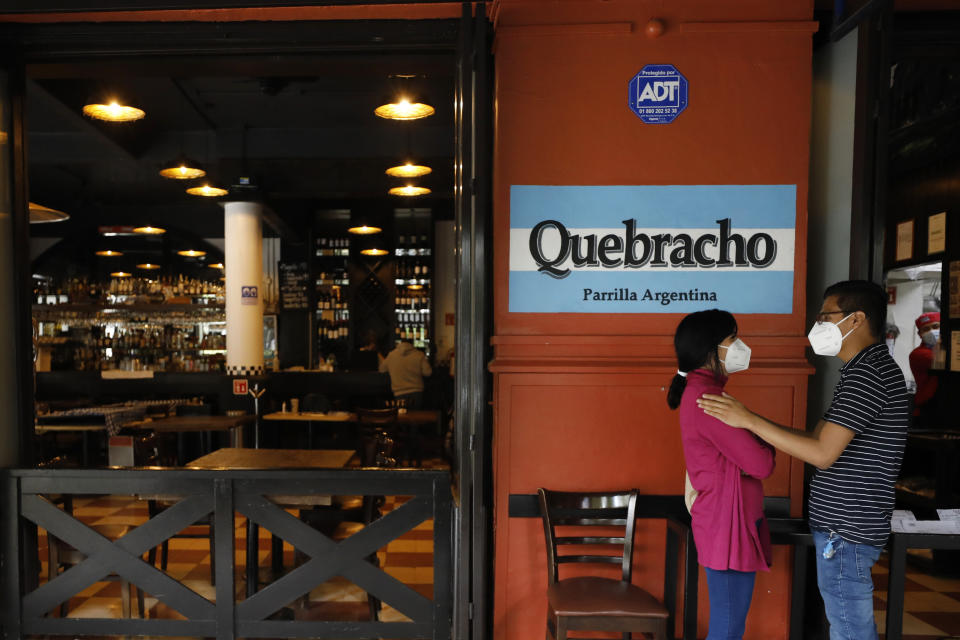 A young couple waits for their takeout order outside Argentine grill Quebracho, in the Cuauhtemoc neighborhood of Mexico City, Sunday, Jan. 10, 2021. Worried about its survival, Quebracho is one of many restaurants in the capital and adjacent Mexico State which are banning together in a campaign dubbed "Abrir o Morir," Spanish for "Open or Die," and plan to open their doors to diners again on Monday in defiance of ordinances limiting restaurants to takeout service while the Mexico Valley remains under a COVID-19 pandemic red alert. (AP Photo/Rebecca Blackwell)