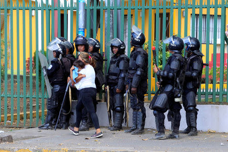 A woman holds her child as she walks past riot police during a protest against reforms that implement changes to the pension plans of the Nicaraguan Social Security Institute (INSS) in Managua, Nicaragua April 19,2018. REUTERS/Oswaldo Rivas