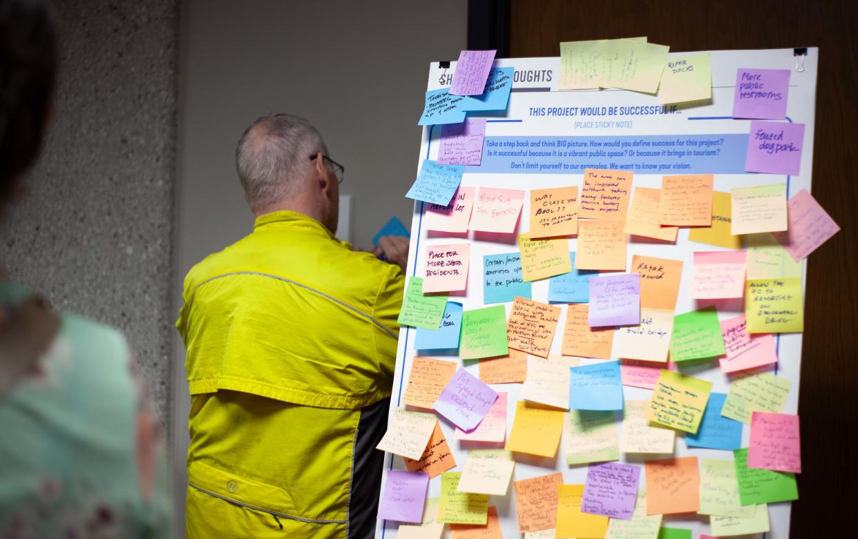 A man writes an idea on a blue sticky note for a full poster of suggestions, as seen, Tuesday, April 30, in Sheboygan, Wis.