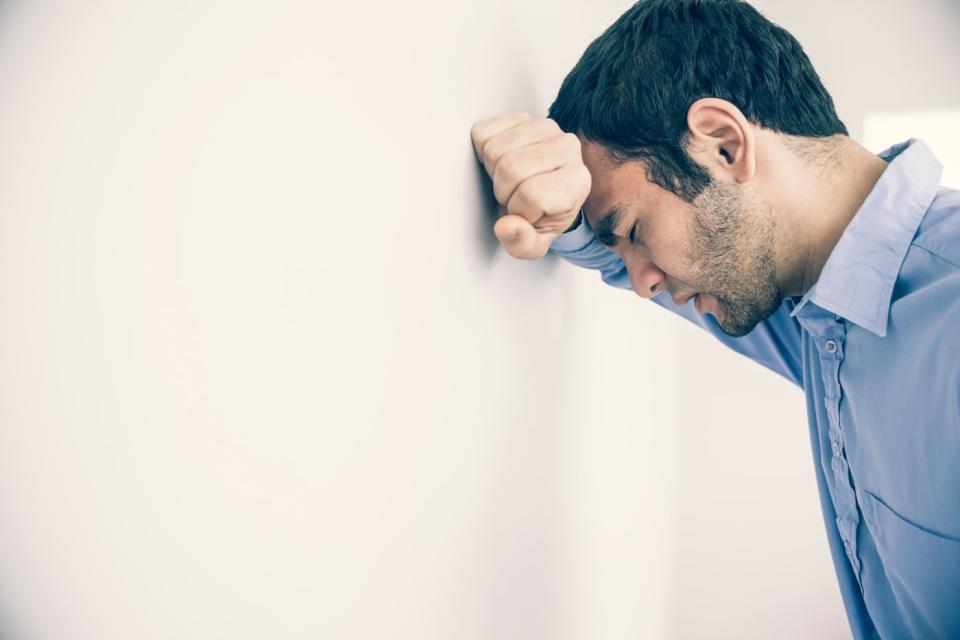 Depressed man with fist clenched leaning his head against a wall