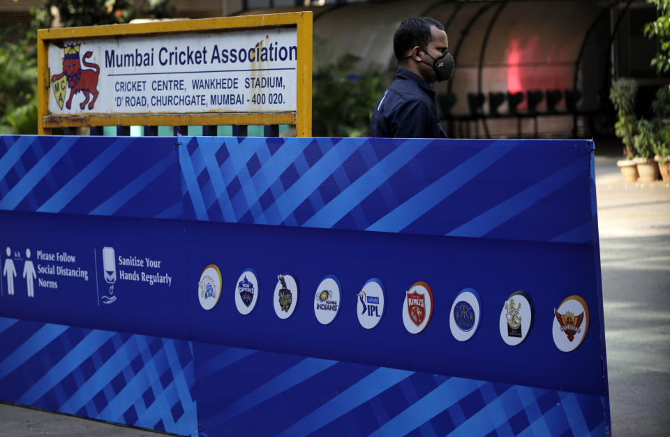 A security guard wearing a face mask as a precaution against the coronavirus stands next to a hoarding displaying logos of teams participating in Indian Premier League 2021, outside Wankhede Stadium in Mumbai, India, Tuesday, May 4, 2021. The Indian Premier League was suspended indefinitely on Tuesday after players or staff at three clubs tested positive for COVID-19 as nationwide infections surged. (AP Photo/Rajanish kakade)