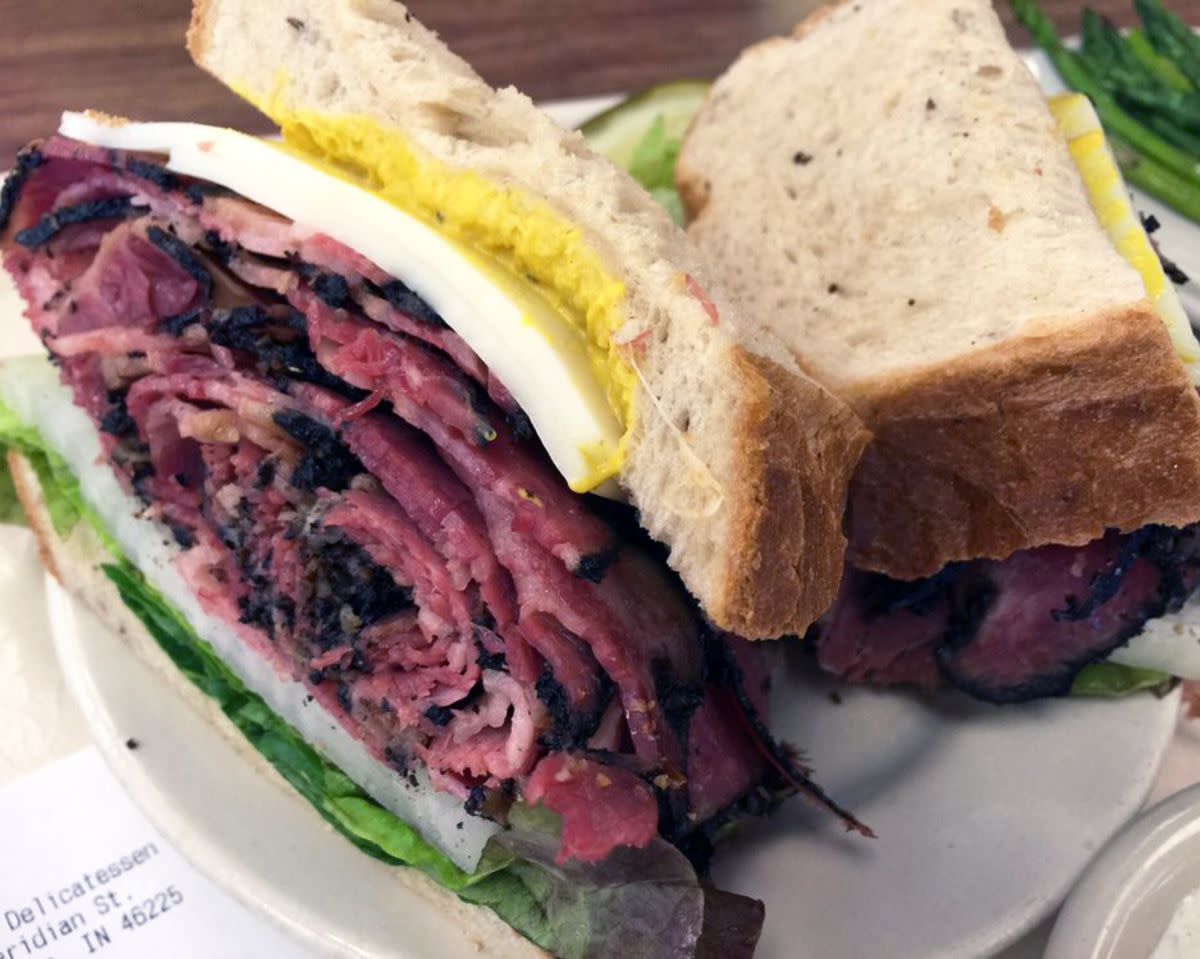 Closeup of Peppered Beef Sandwich on a white ceramic plate, Shapiro's Delicatessen, Indianapolis, a side of asparagus on the far right, on a veneer wooden table