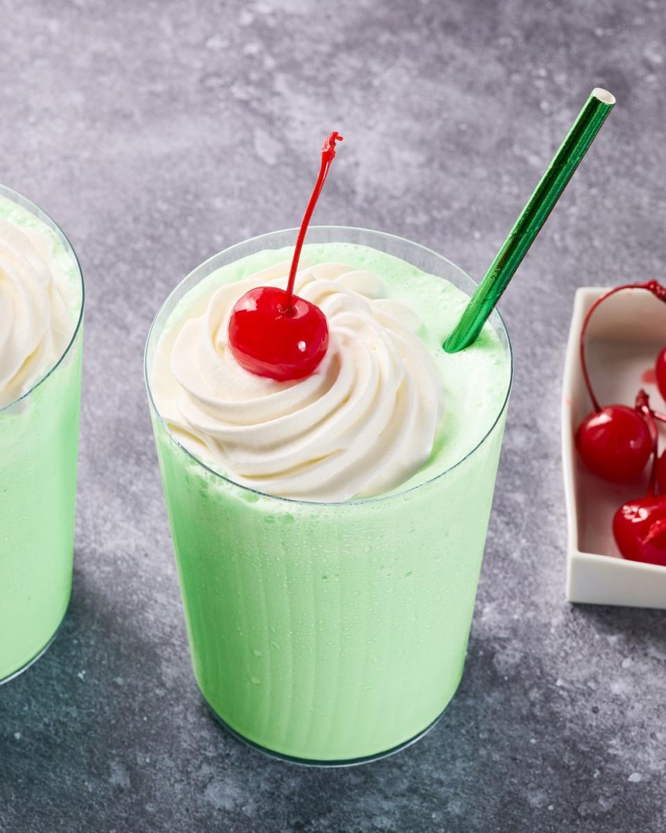 green shake in a glass with whipped cream, a cherry, and a green straw