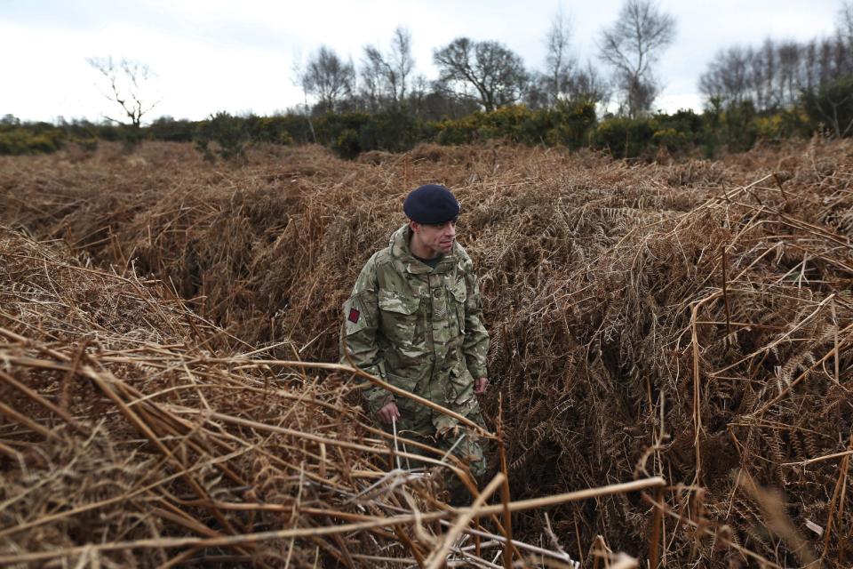 A British army officer walks on a WW1 practise trench as he poses for the photographers in Gosport, southern England, Thursday, March 6, 2014. This overgrown and oddly corrugated patch of heathland on England’s south coast was once a practice battlefield, complete with trenches, weapons and barbed wire. Thousands of troops trained here to take on the Germany army. After the 1918 victory _ which cost 1 million Britons their lives _ the site was forgotten, until it was recently rediscovered by a local official with an interest in military history. Now the trenches are being used to reveal how the Great War transformed Britain _ physically as well as socially. As living memories of the conflict fade, historians hope these physical traces can help preserve the story of the war for future generations. (AP Photo/Lefteris Pitarakis)
