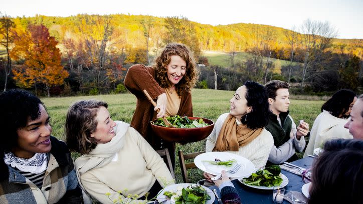 woman serving salad to friends at dinner party