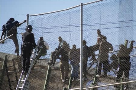 African migrants sit on top of a border fence during an attempt to cross into Spanish territories, between Morocco and Spain's north African enclave of Melilla, November 21, 2015. REUTERS/Jesus Blasco de Avellaneda/Files