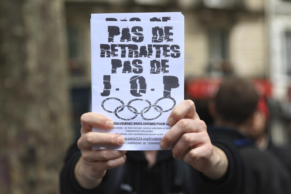 An activist shows a leaflet reading "No withdrawal of the pension reform, no Olympic Games" in Paris, Monday, May 1, 2023. Olympic contestation is picking up online and starting to spill onto streets, because protesters are linking the Paris Games to unpopular pension reforms pushed through by French President Emmanuel Macron. (AP Photo/Aurelien Morissard)