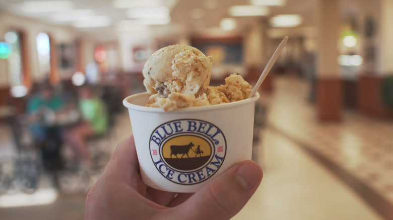 a hand holding up a scoop of Blue Bell ice cream in a cup