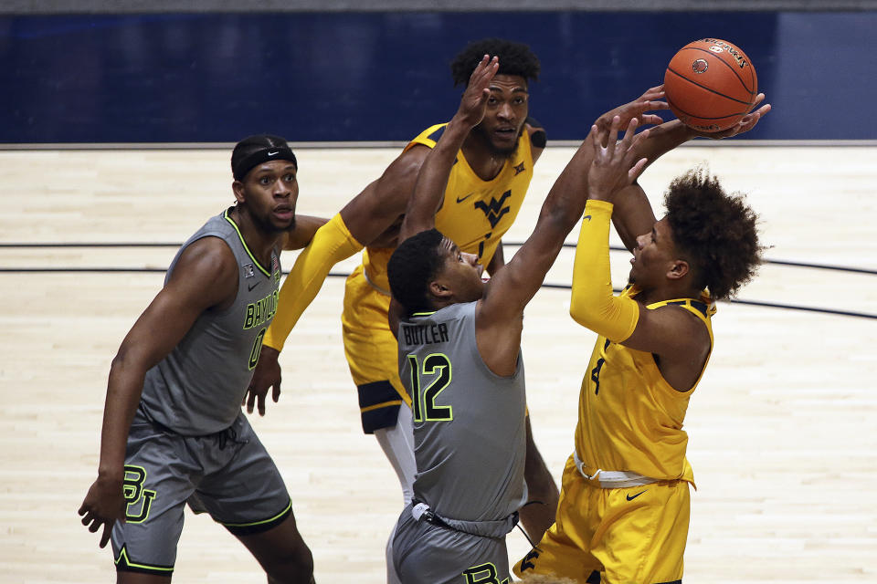 West Virginia guard Miles McBride (4) shoots while defended by Baylor guard Jared Butler (12) and West Virginia forward Derek Culver (1) and Baylor forward Flo Thamba (0) look on during the first half of an NCAA college basketball game Tuesday, March 2, 2021, in Morgantown, W.Va. (AP Photo/Kathleen Batten)