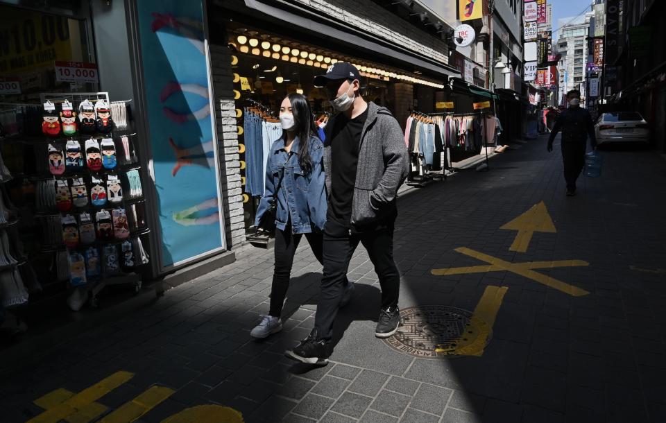 A couple wearing face masks walk through a shopping district in Seoul on April 23, 2020. (Photo: JUNG YEON-JE via Getty Images)