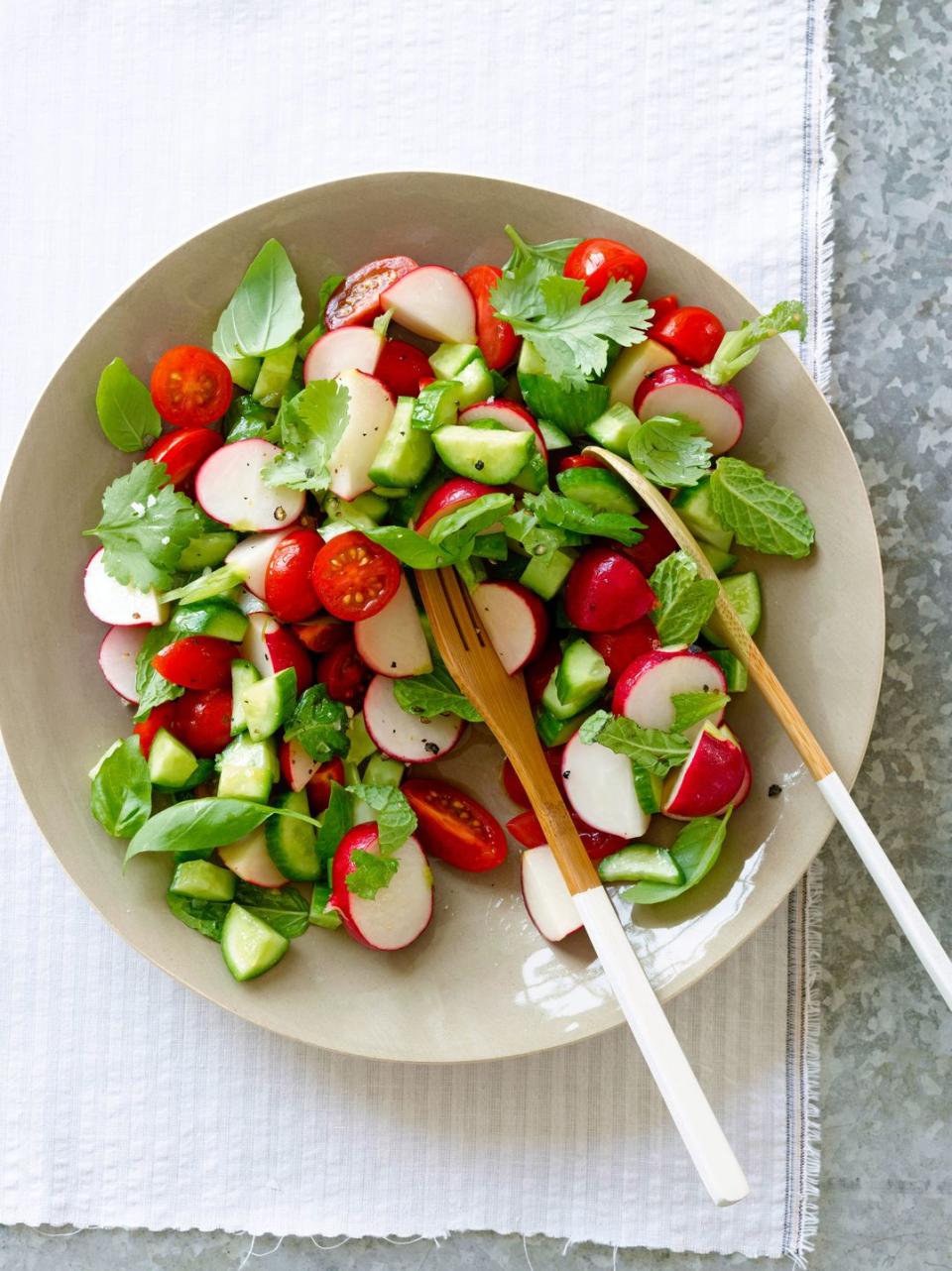 a bowl of radish salad with greens and tomatoes on a white plate