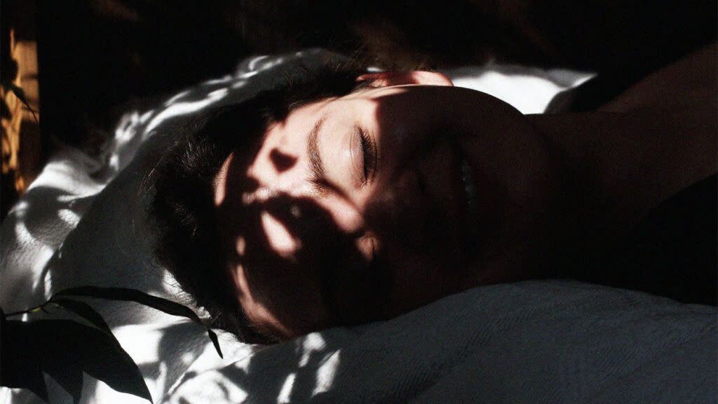 A woman sleeps in bed with shadows on her smiley face