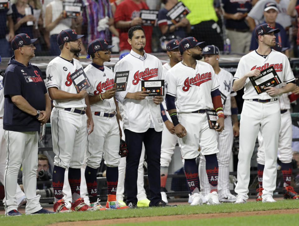FILE - In this July 9, 2019, file photo, Cleveland Indians pitcher Carlos Carrasco, center without a hat, stands with Indians teammates during the fifth inning of the baseball All-Star Game in Cleveland, as part of Major League Baseball's "Stand Up to Cancer" campaign. Carrasco, who was diagnosed with leukemia and was honored during Tuesday’s, July 9 All-Star Game, will throw a bullpen session and he’s confident he can overcome his condition and pitch again for Cleveland this season. (AP Photo/Tony Dejak, File)