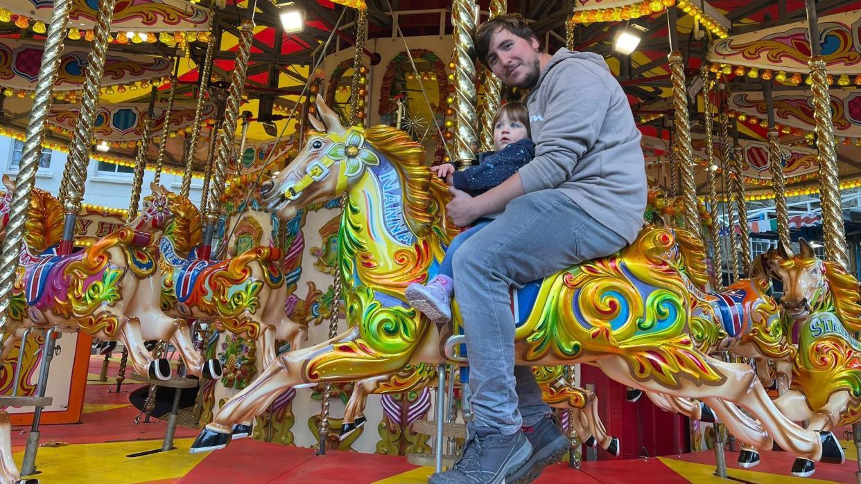 A man and a little girl ride a horse on the merry-go-round.