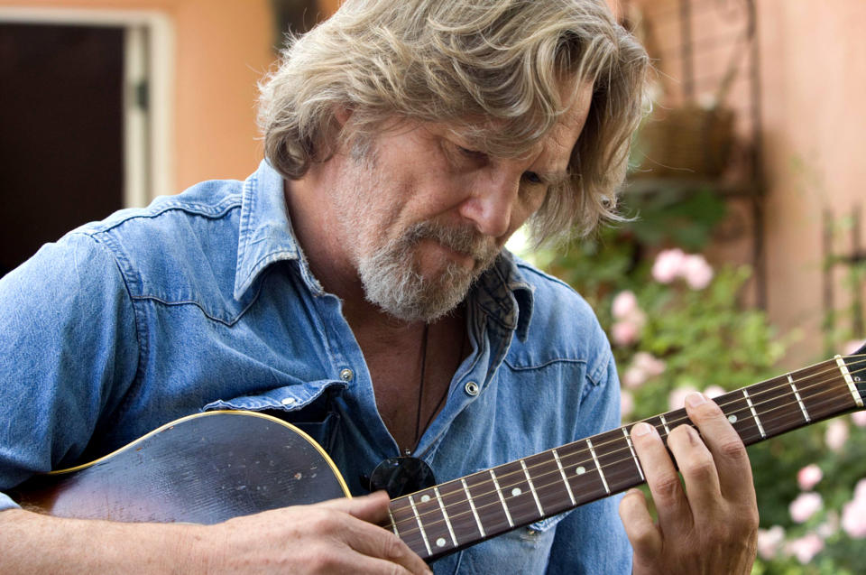 Jeff with a beard playing an acoustic guitar, focused on the strings, wearing a denim shirt